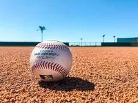 A baseball sits on an infield dirt patch.